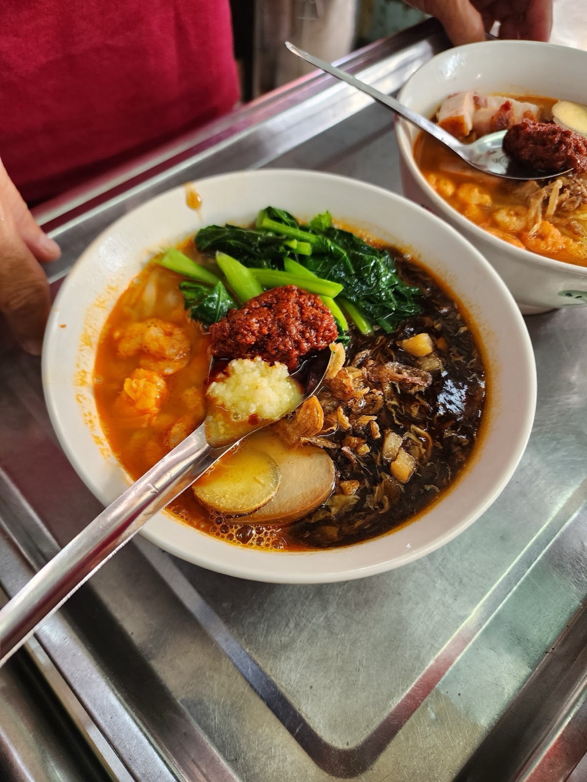 A bowl of dark five-spice loh mee with greens, egg and a spoonful of red sambal