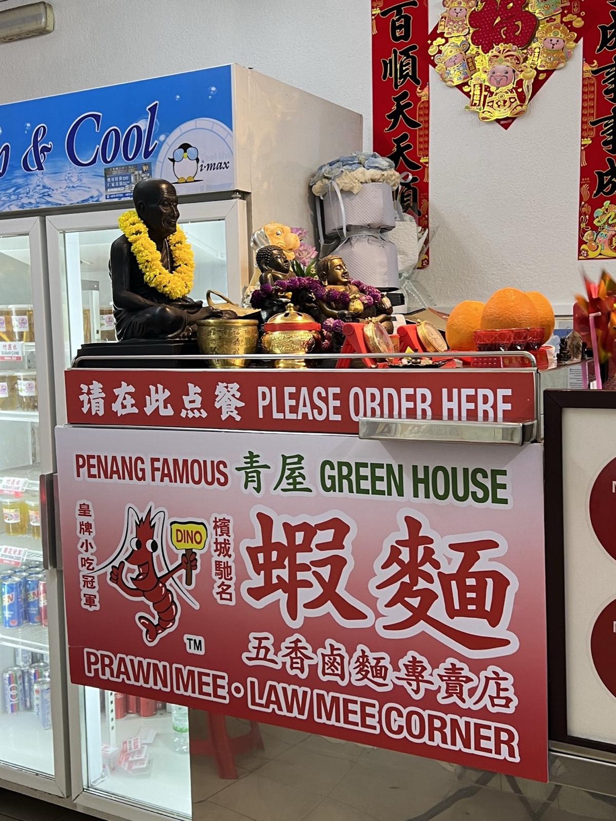 The Please Order Here counter with the red prawn signboard and a small altar above the drinks fridge