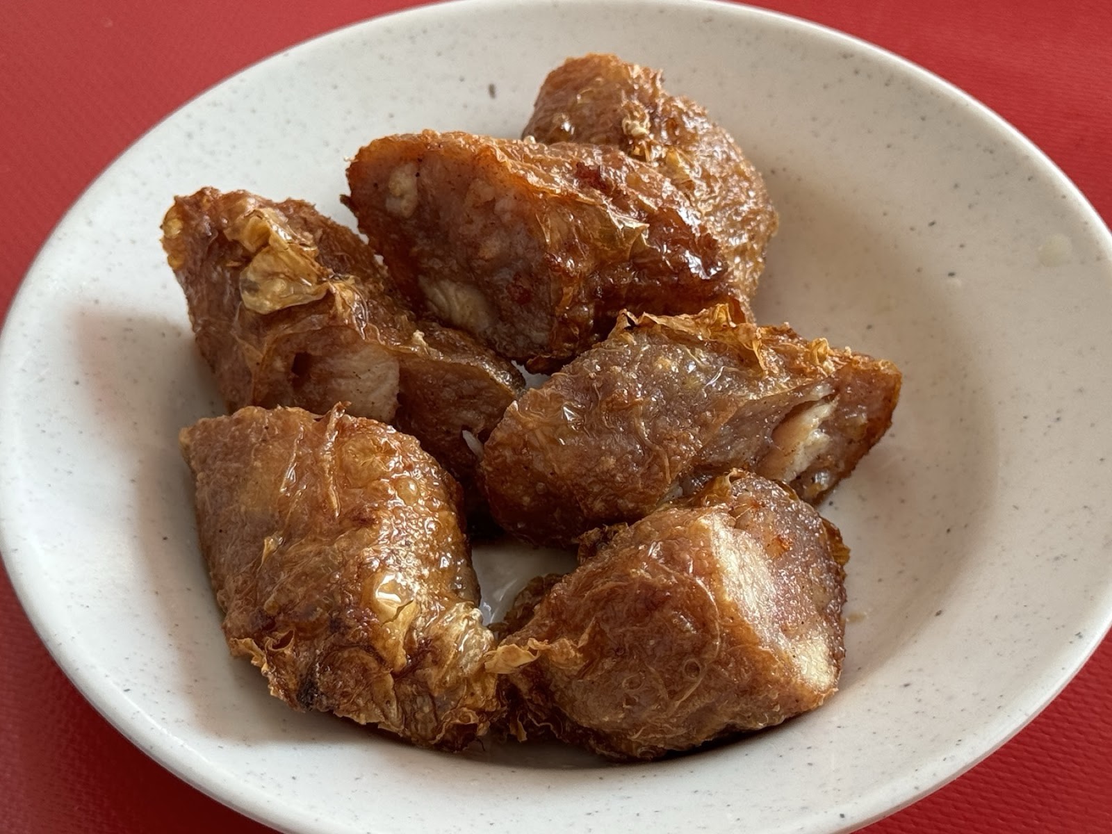 A plate of golden deep-fried loh bak five-spice pork rolls on a cream dish