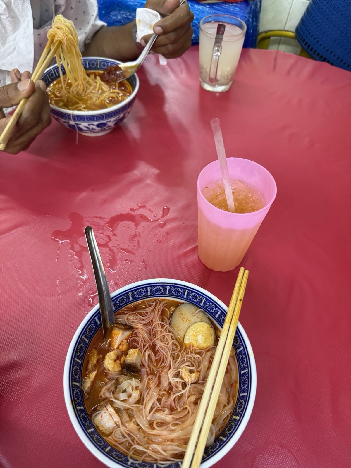 An overhead shot of two prawn mee bowls and a pink cup of iced drink on a red dining table